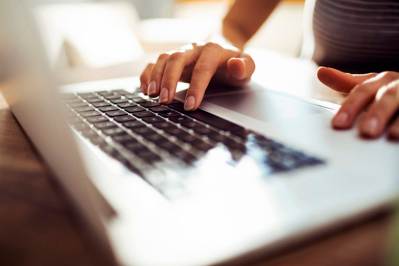 Close up of hands typing at a laptop keyboard.