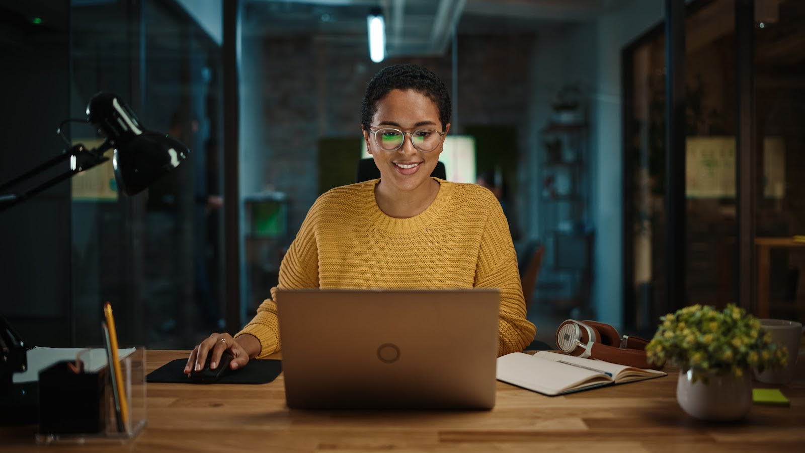 A woman works at a laptop computer in a busy creative office environment.