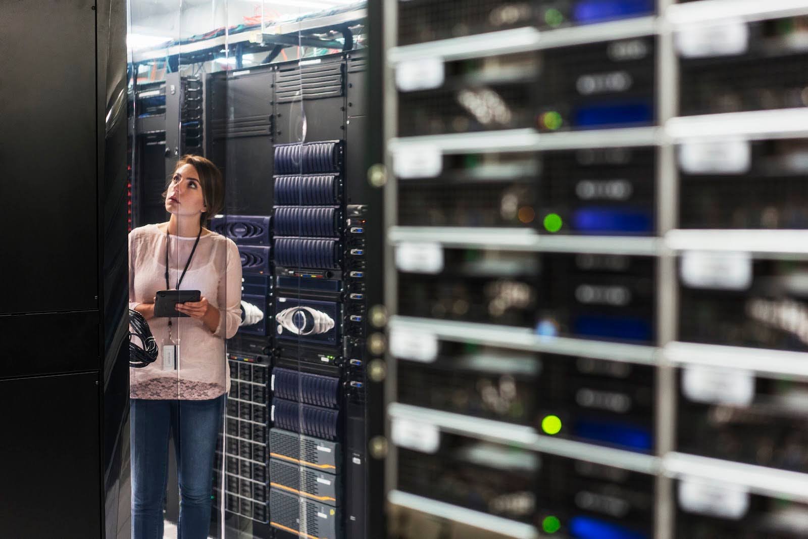 A computer scientist in a server room uses a tablet.