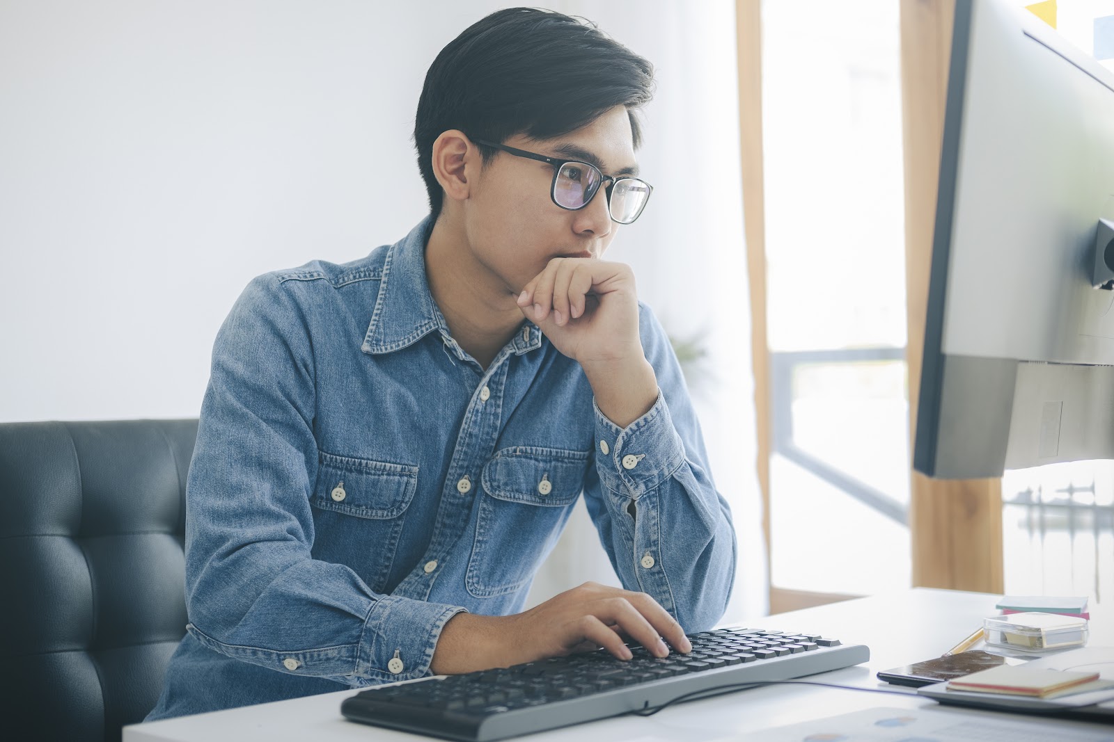 A male computer science professional in an office focuses on a computer screen.